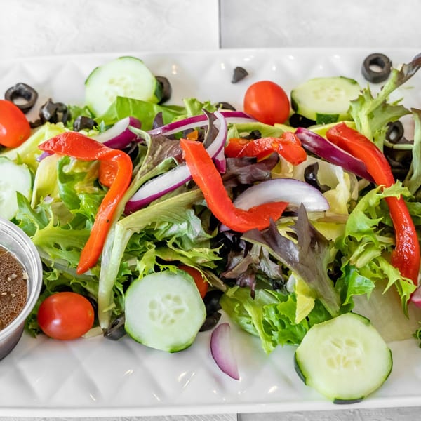 A fresh garden salad with mixed greens, red peppers, cucumbers, tomatoes, red onion, and black olives.