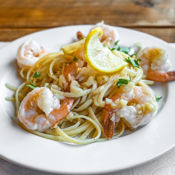 Shrimp scampi with linguine, garlic, parsley, and lemon wedges on a white plate.