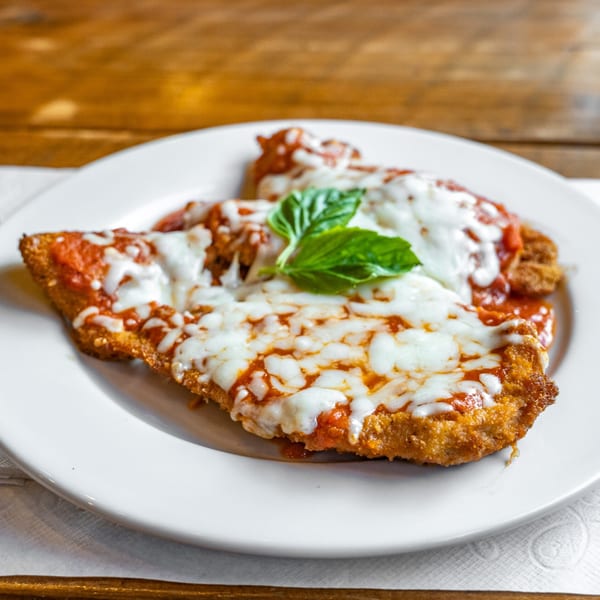 Chicken Parmesan with melted mozzarella, marinara sauce, and fresh basil on a white plate.