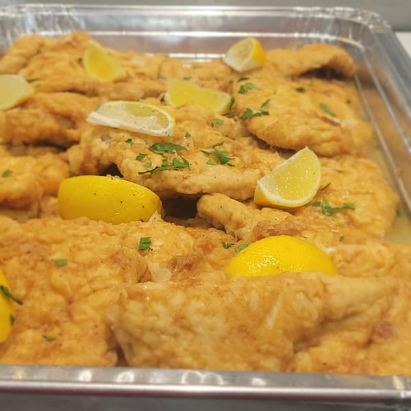 Chicken piccata with lemon slices and parsley in a silver serving tray.