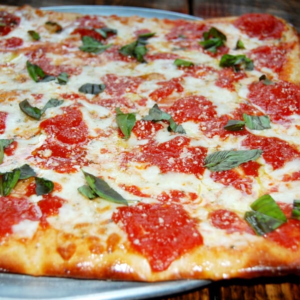 Danny's Pizzeria's rectangular pizza with melted mozzarella, red sauce, and fresh basil leaves.