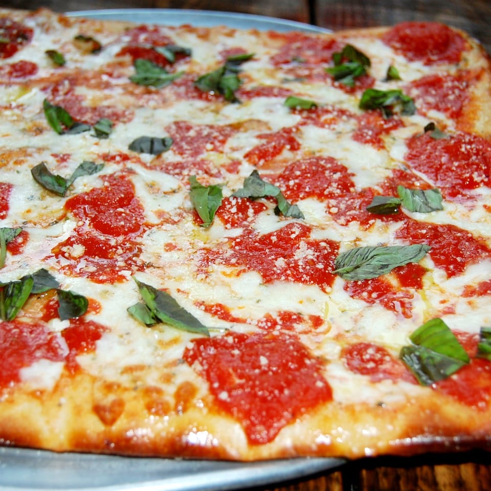 Danny's Pizzeria's rectangular pizza with melted mozzarella, red sauce, and fresh basil leaves.