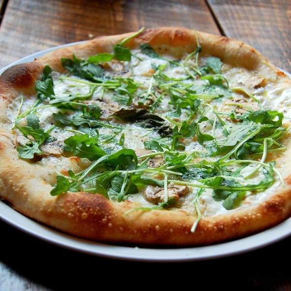 Danny's Pizzeria white pizza with mushrooms and arugula on a rustic wooden table.