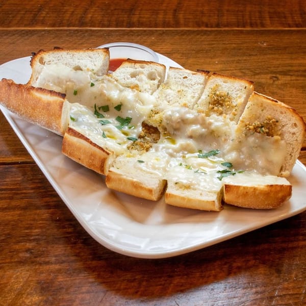 Cheesy garlic bread, cut into slices, topped with parsley, served on a white plate with sauce.