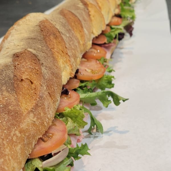 A long submarine sandwich with lettuce, tomatoes, onions, and deli meat on a white surface.
