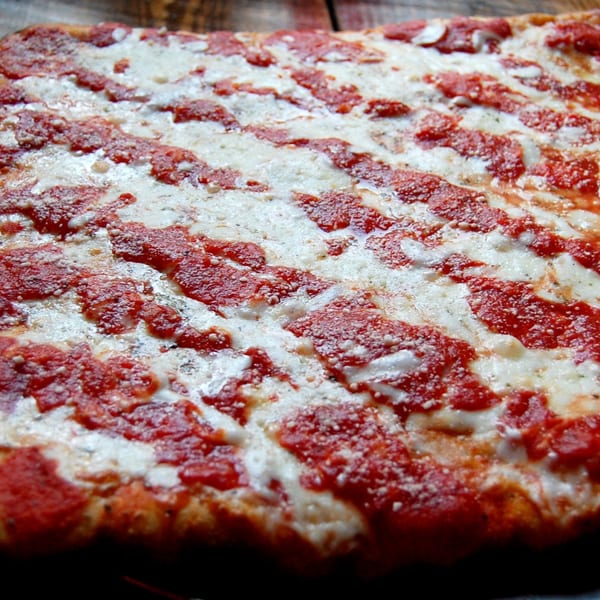 Close-up of a rectangular Danny's Pizzeria pizza with stripes of red sauce and white cheese.