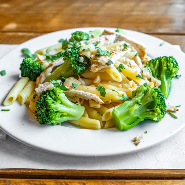 Penne pasta with chicken, broccoli florets, and parsley on a white plate.