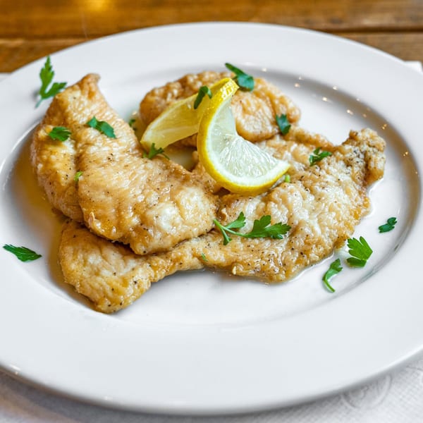 Chicken piccata with lemon wedges and parsley on a white plate at Danny's Pizzeria.