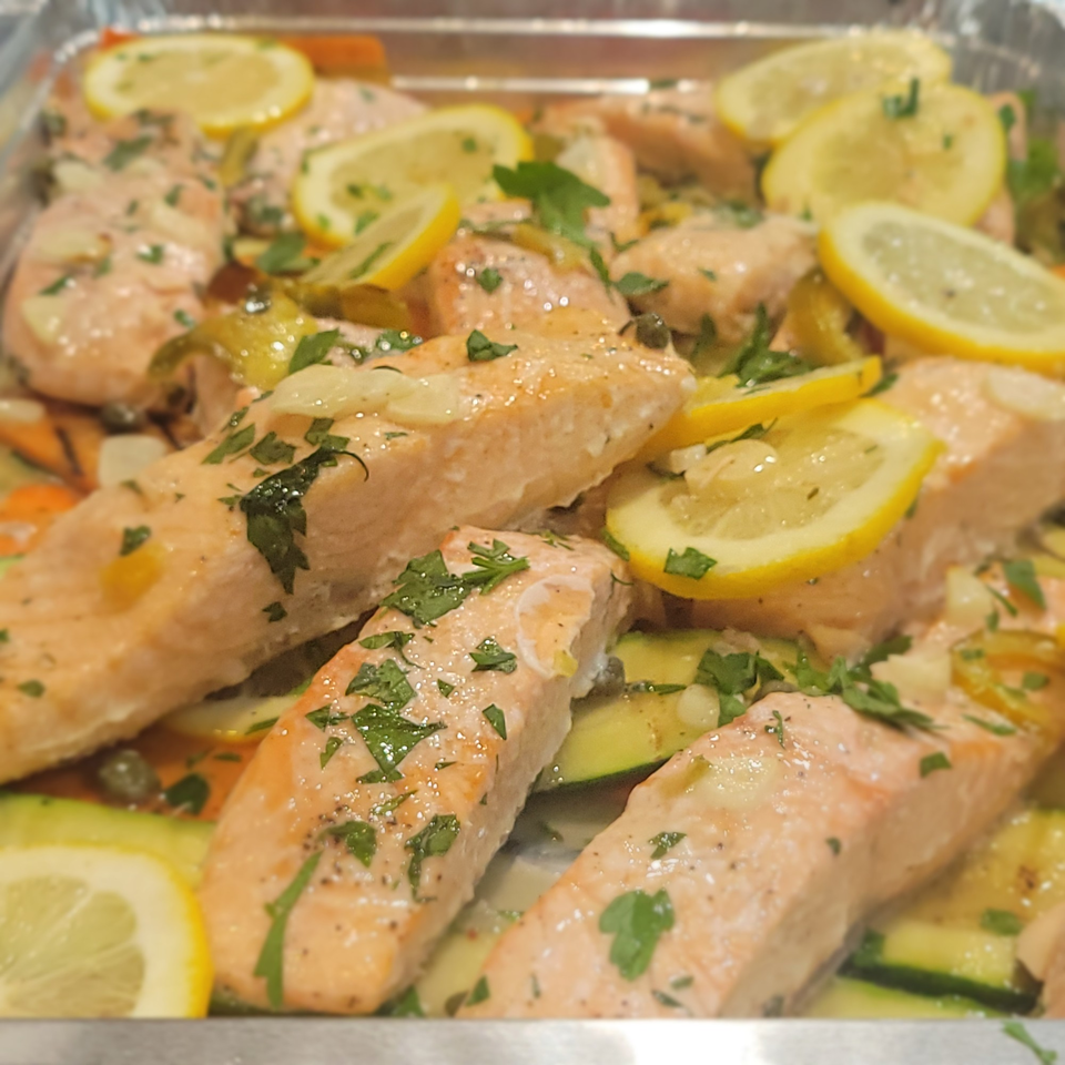 Baked salmon fillets with lemon slices, zucchini, and parsley in a silver pan.