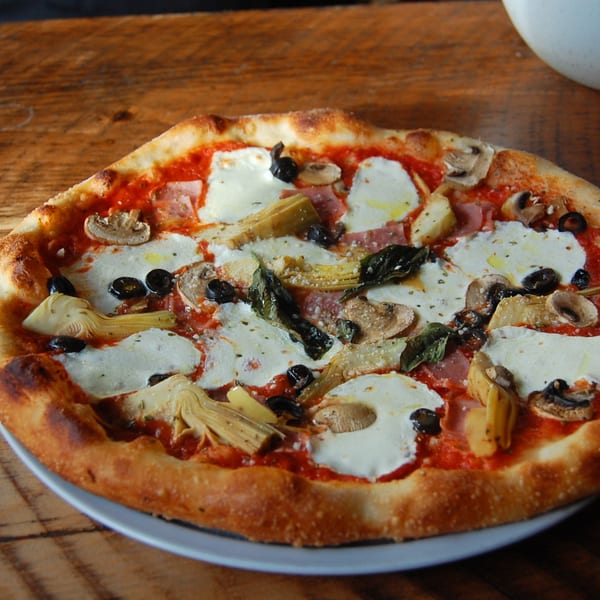 Danny's Pizzeria pizza with fresh mozzarella, artichokes, mushrooms, olives, and basil on a wooden table.