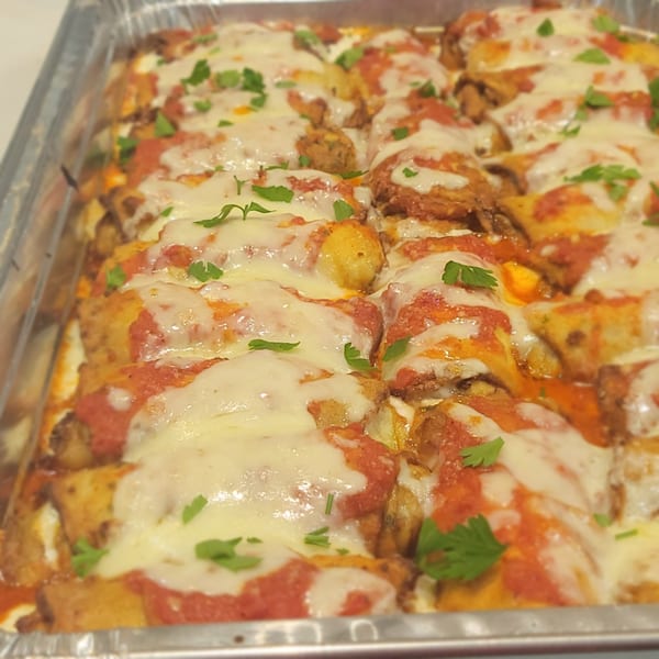Baked pasta dish with melted mozzarella, red sauce, and fresh parsley in a foil pan.