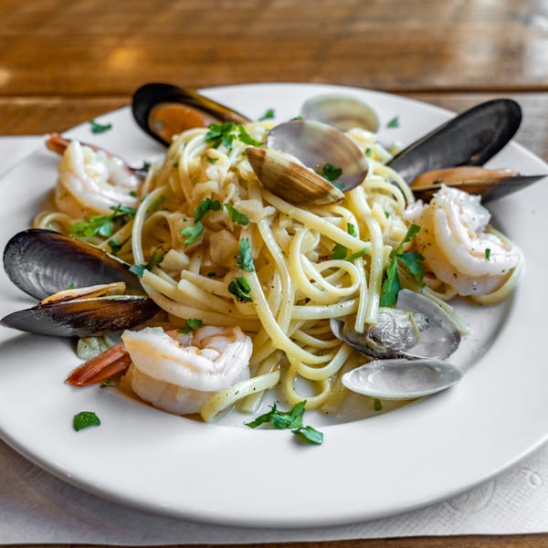 Linguine pasta with shrimp, mussels, and clams, garnished with parsley on a white plate.