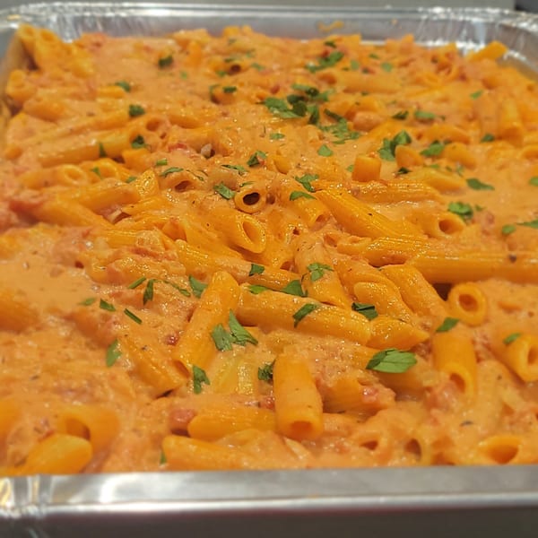 Penne pasta in a creamy tomato sauce with fresh parsley, served in a foil tray.