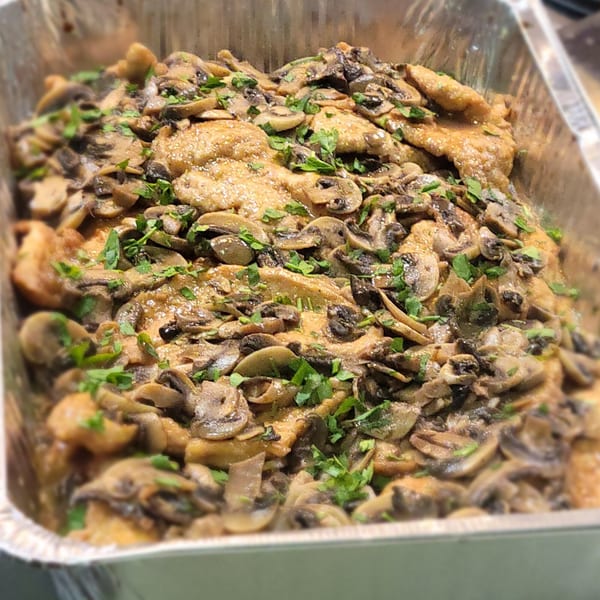 Chicken and mushrooms in a creamy sauce, garnished with parsley, in a metal serving tray.