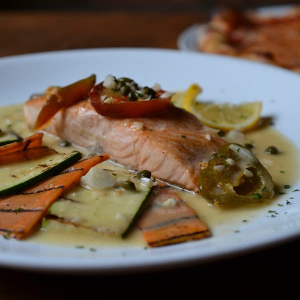 Salmon fillet with grilled vegetables, cherry tomatoes, capers, and lemon in a light sauce.