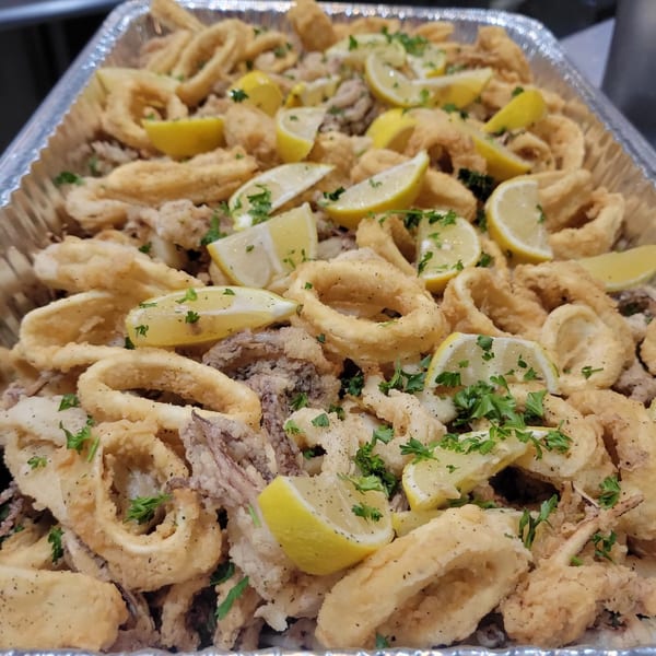 A catering tray filled with golden-fried calamari rings and tentacles, garnished with lemon wedges and parsley.